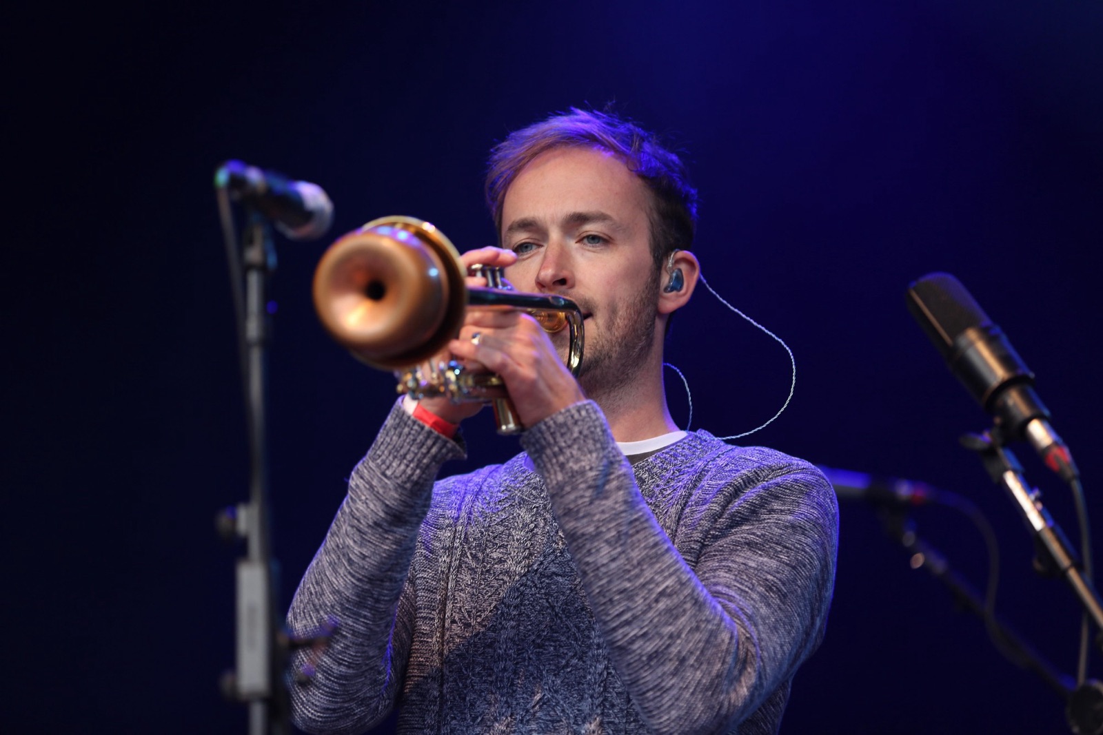 Thomas Hodgson playing trumpet on stage under blue light, with microphones either side.